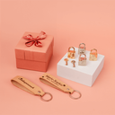 Personalisierte Geschenke: gravierte Vorhängeschlösser, Schlüssel & Lederanhänger mit Geschenkbox auf Pfirsich-Hintergrund